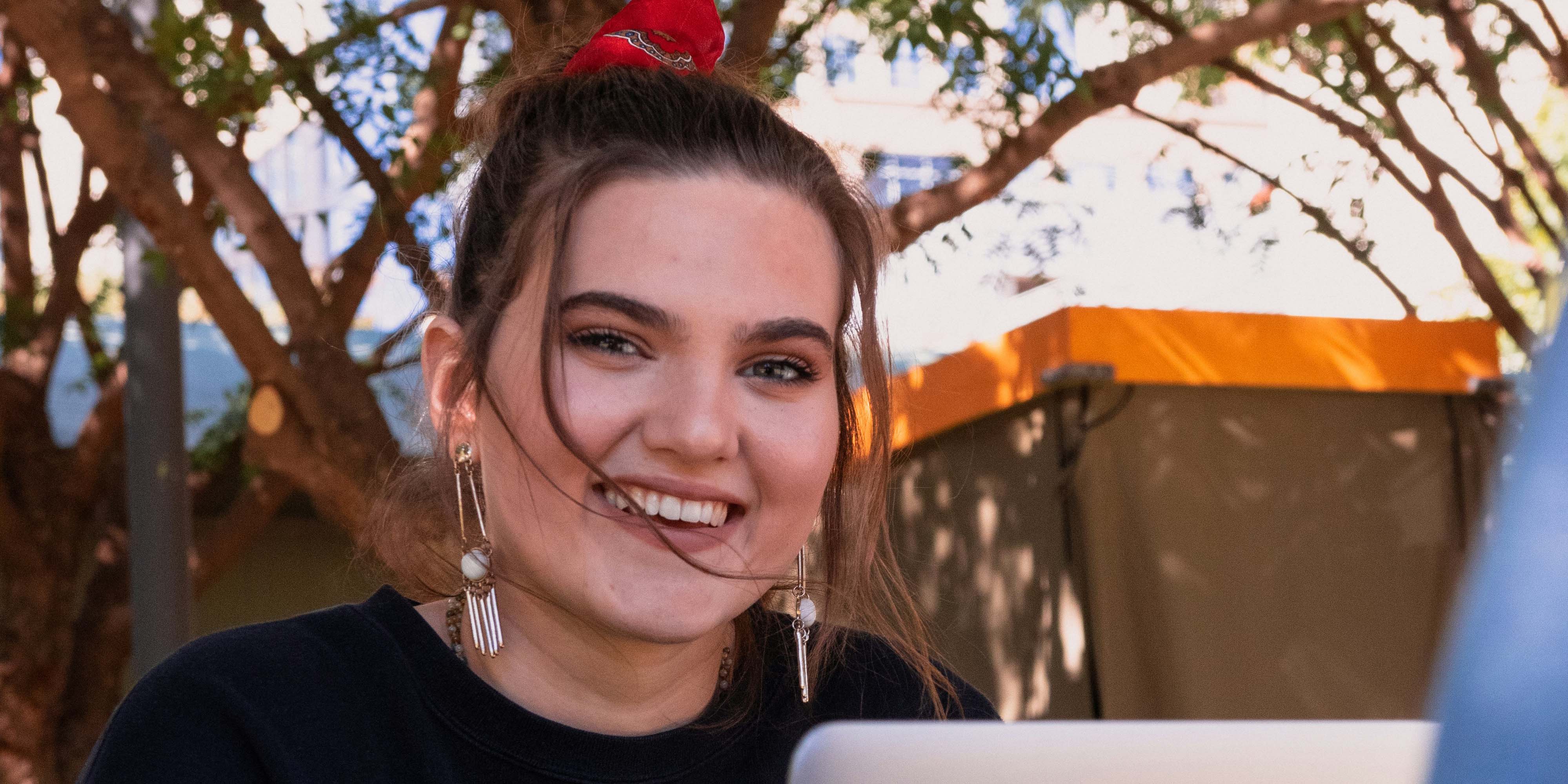 Auf dem Foto ist eine junge Frau zu sehen, die hinter ihrem Laptop sitzt und lächelt.