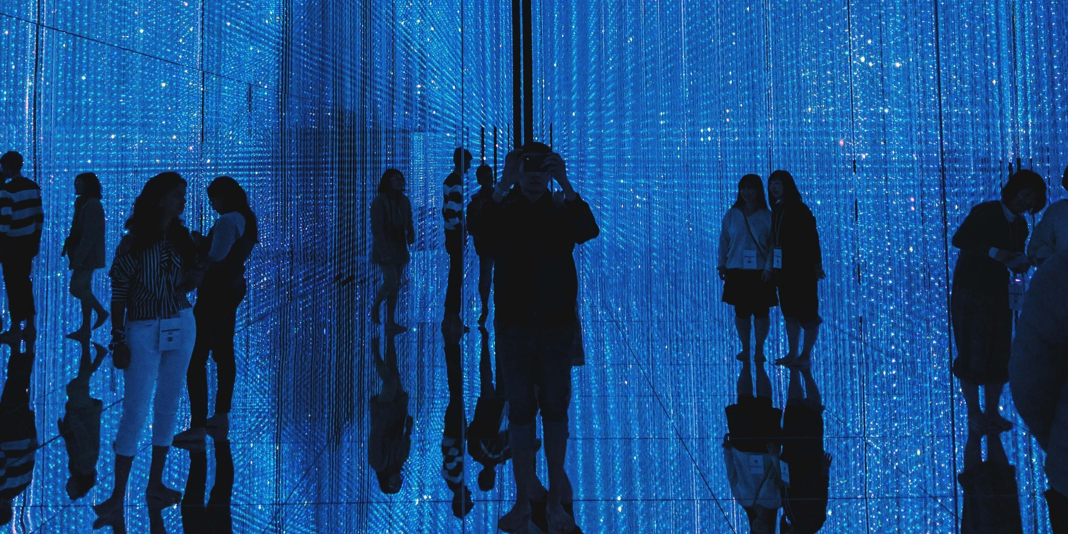 Auf dem Bild sind Menschen zu sehen, die in einem blau verpixelten Raum herumgehen.