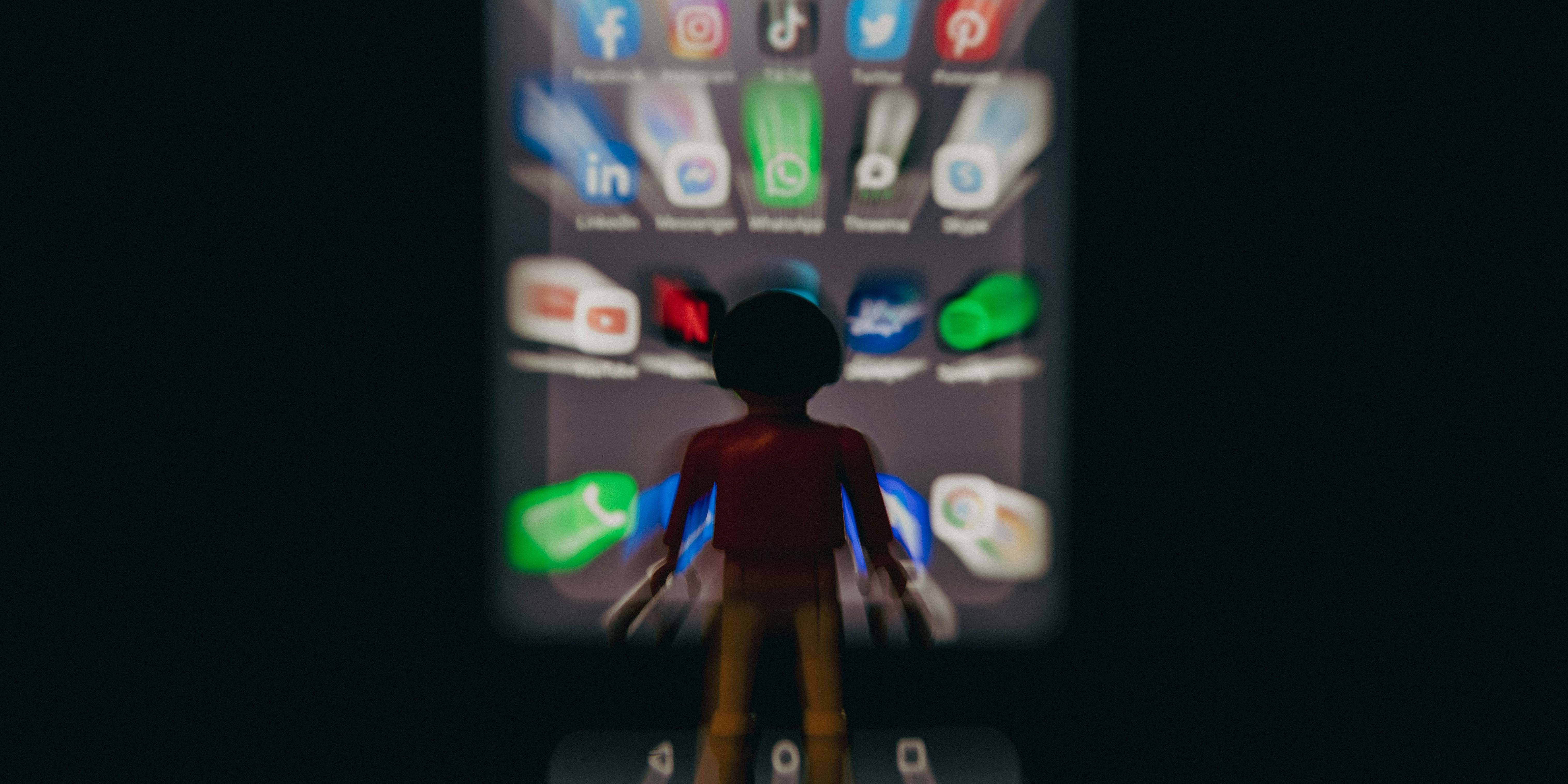 Auf dem Foto steht ein Playmobil Männchen vor einem Smartphone Bildschirm, auf dem man lauter Social Media und sozialer Netzwerke Apps sieht, wie Facebook und WhatsApp.