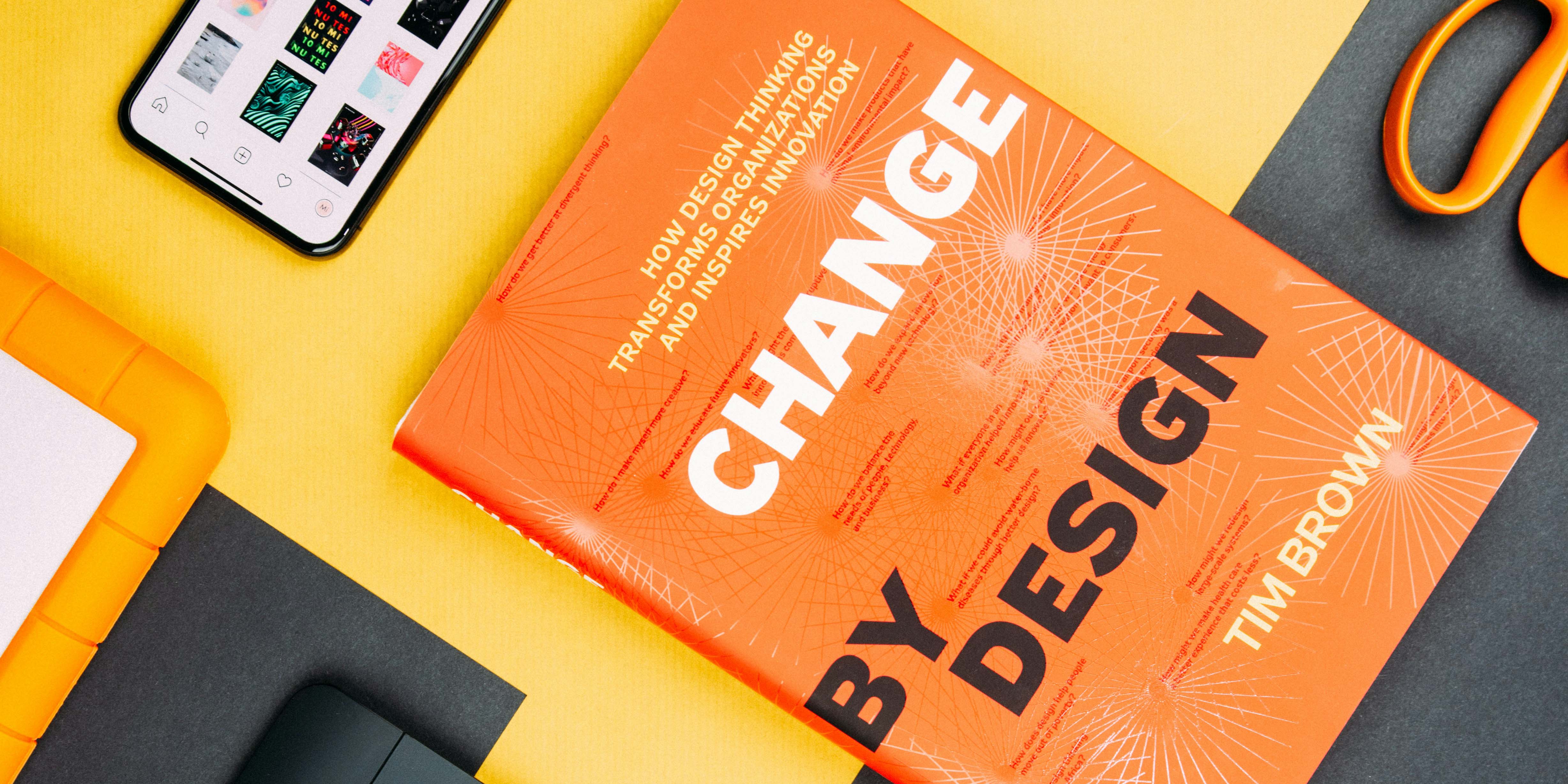 Auf dem Bild ist ein Schreibtisch zu sehen, auf dem u.a. ein Smartphone, eine Schere und ein Buch liegen. Das Buch trägt den Titel "Change by Design".