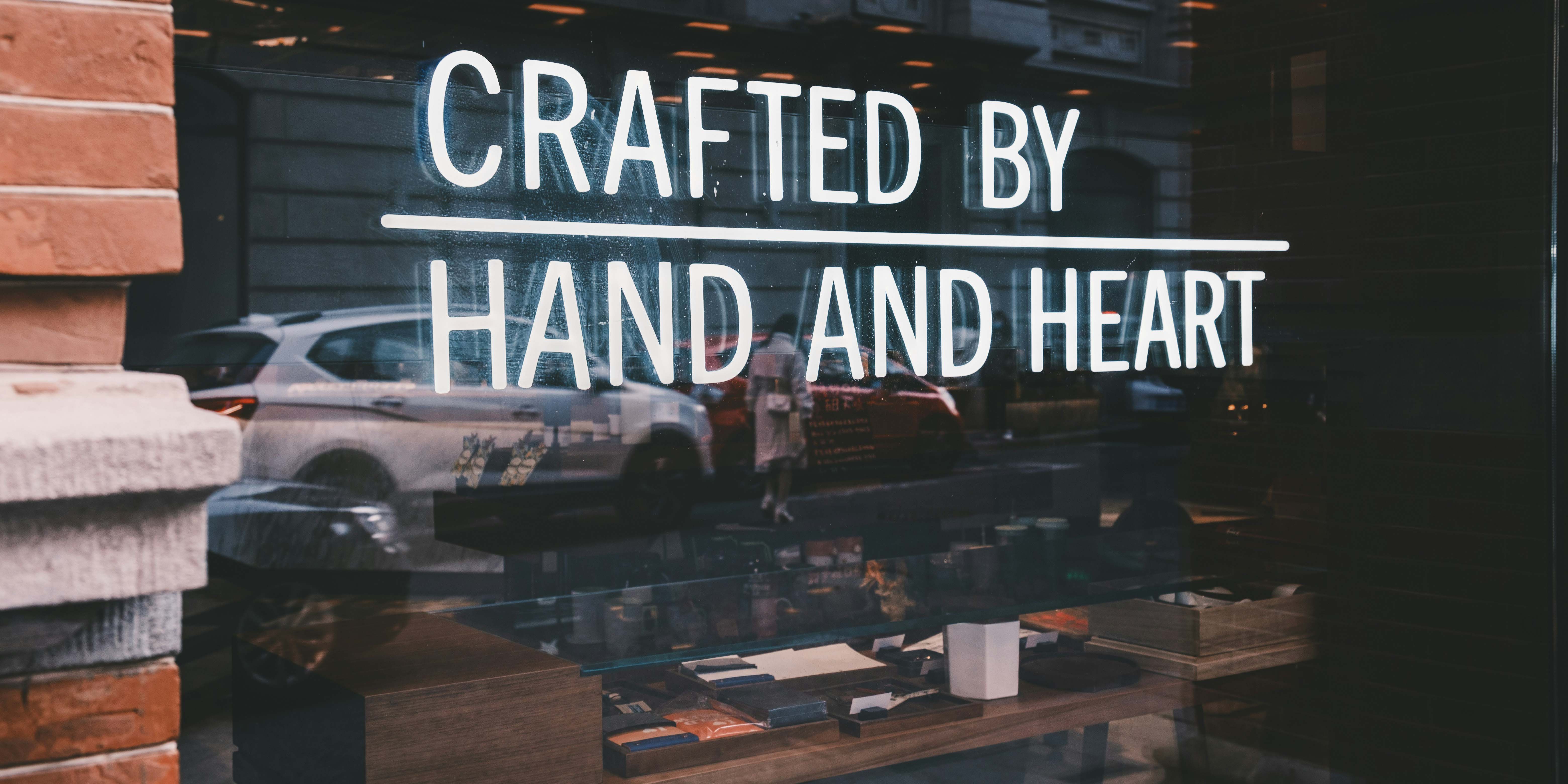 Auf dem Foto ist ein Schaufenster zu sehen. Auf diesem steht: Crafted by hand and heart.